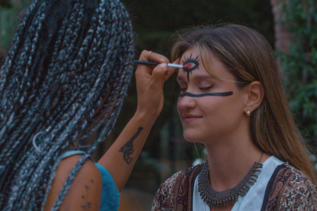 A young woman is having her face painted at an Ayahuasca retreat